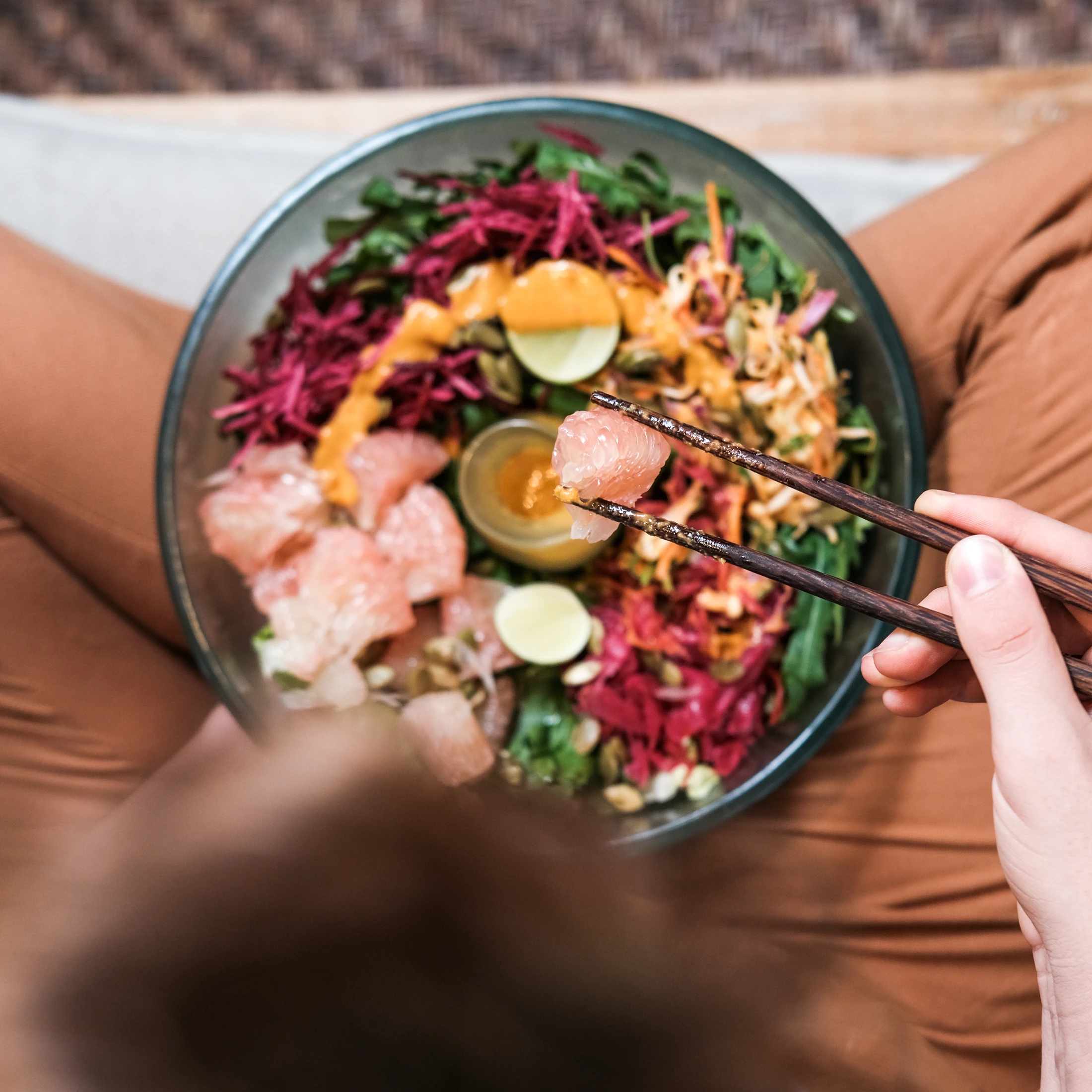 A diner lifts a citrus segment with chopsticks above a colourful plant-based bowl at Alchemy.