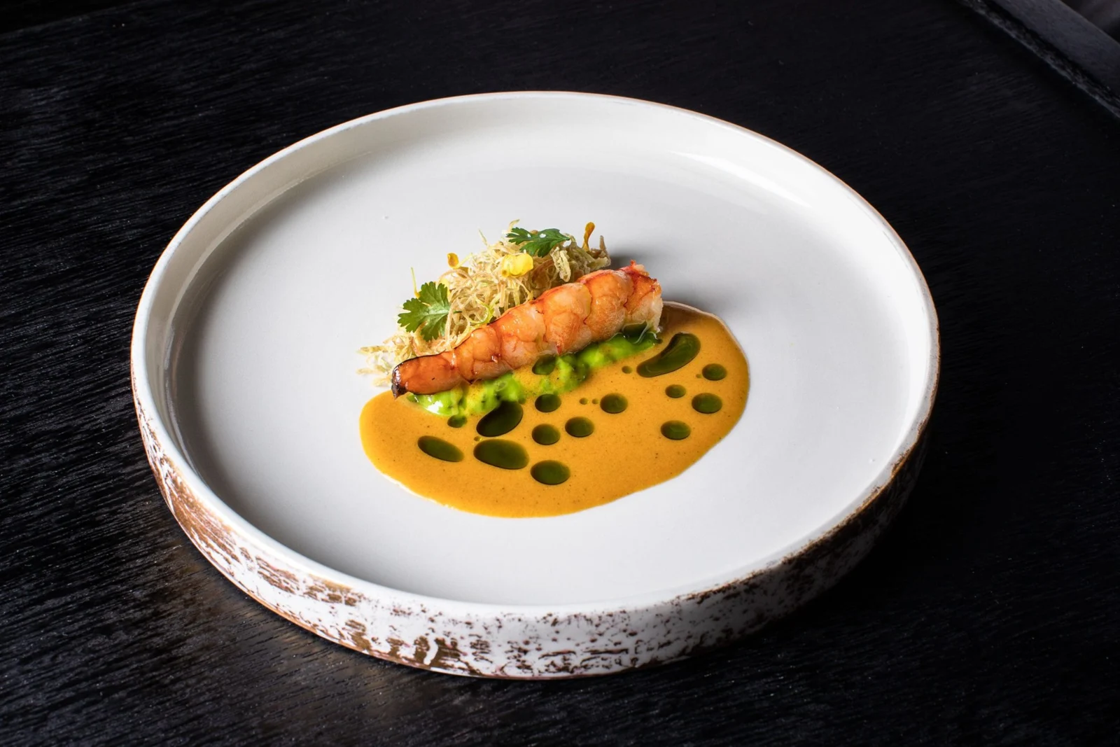 An Apéritif tasting-menu course plated with orange sauce and fresh green garnish.