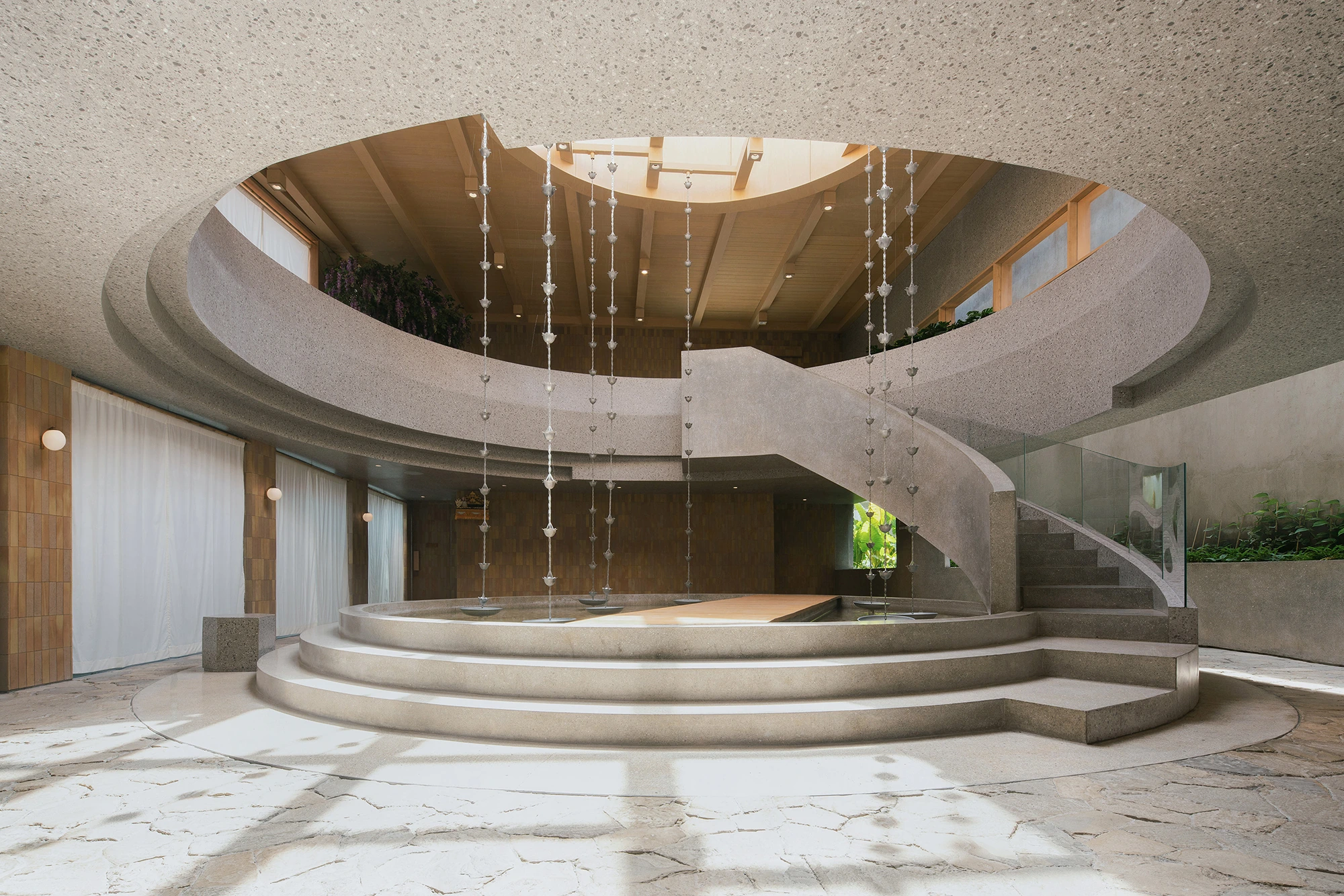 Curved terrazzo galleries, hanging rain chains and a shallow pond inside Café 32do in Seminyak.