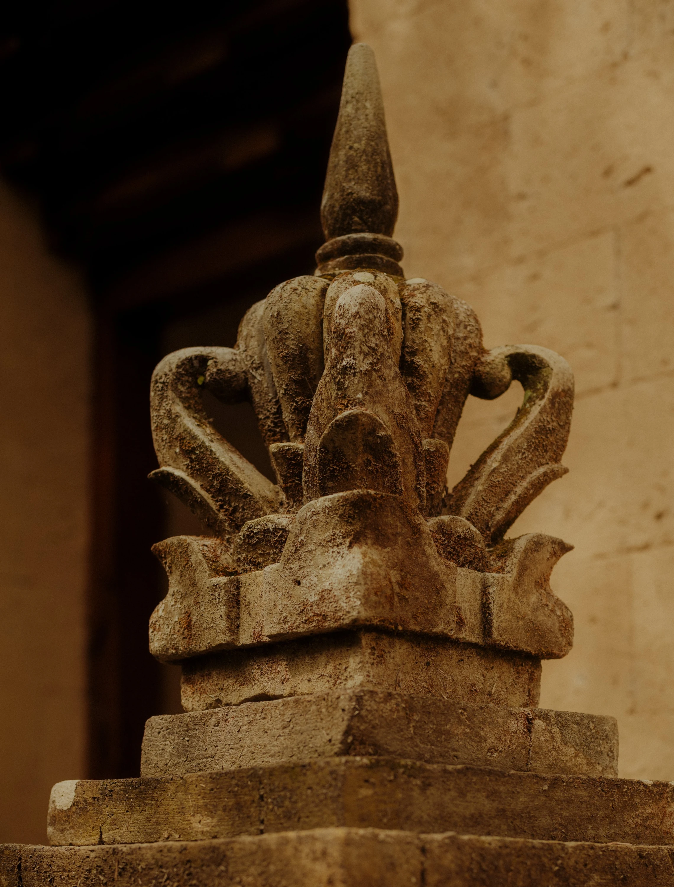A weathered carved stone finial against a warm wall at Amandari.