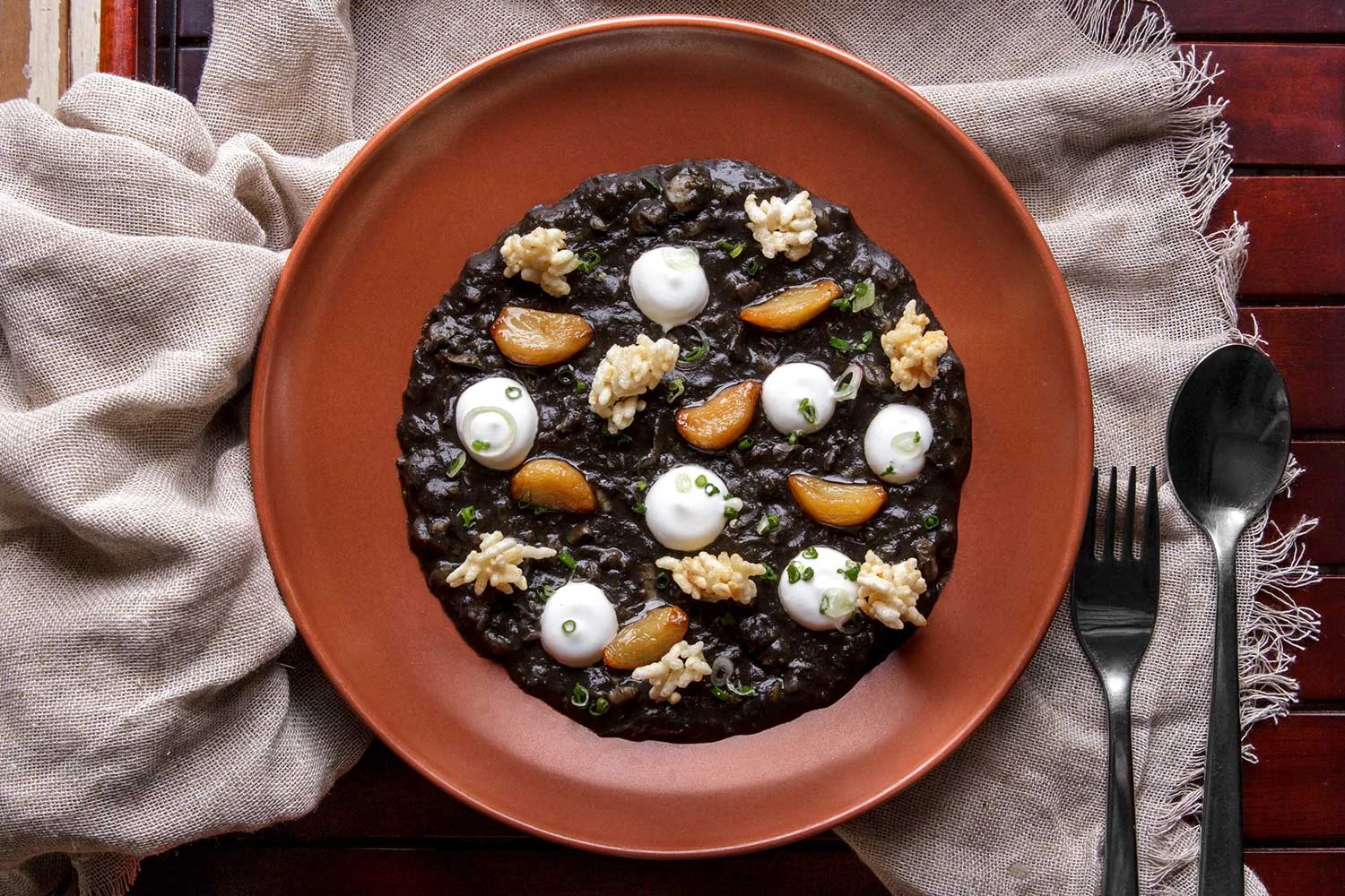 A dark rice dish served on a terracotta plate at Cuca