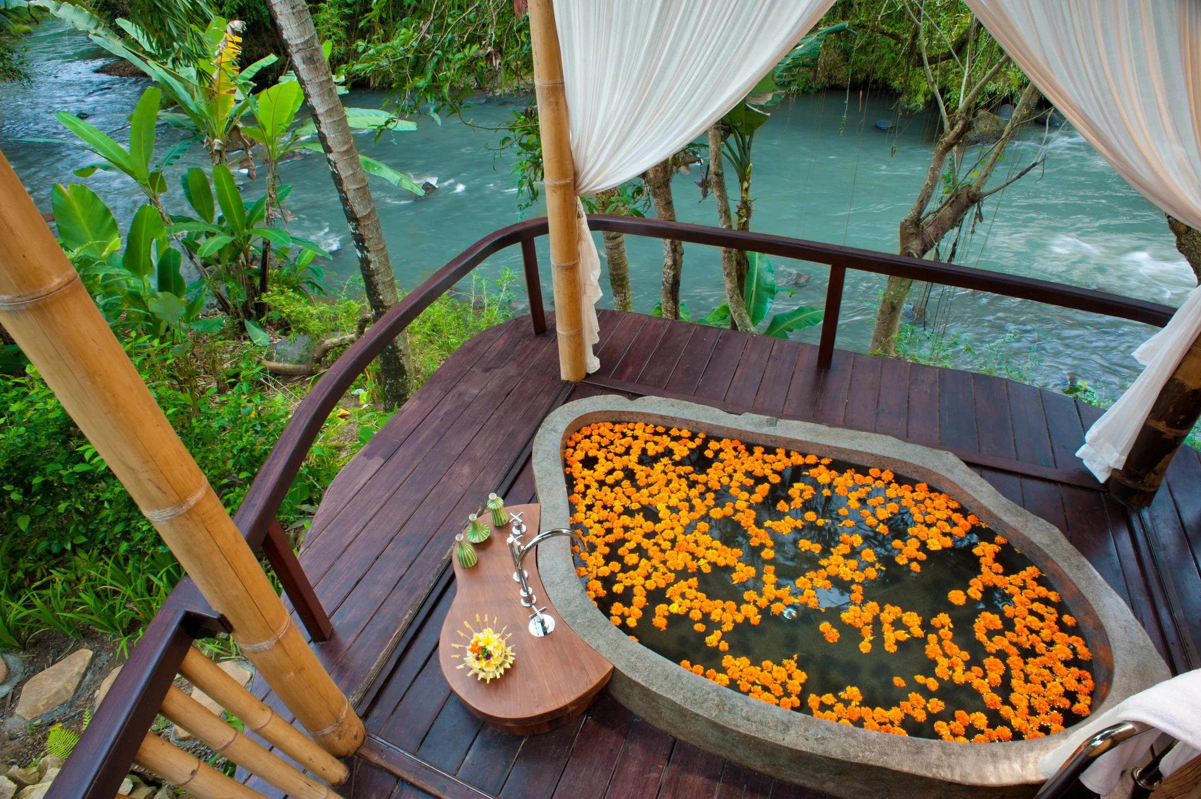 An oval bath filled with orange flowers overlooking the river at Fivelements.