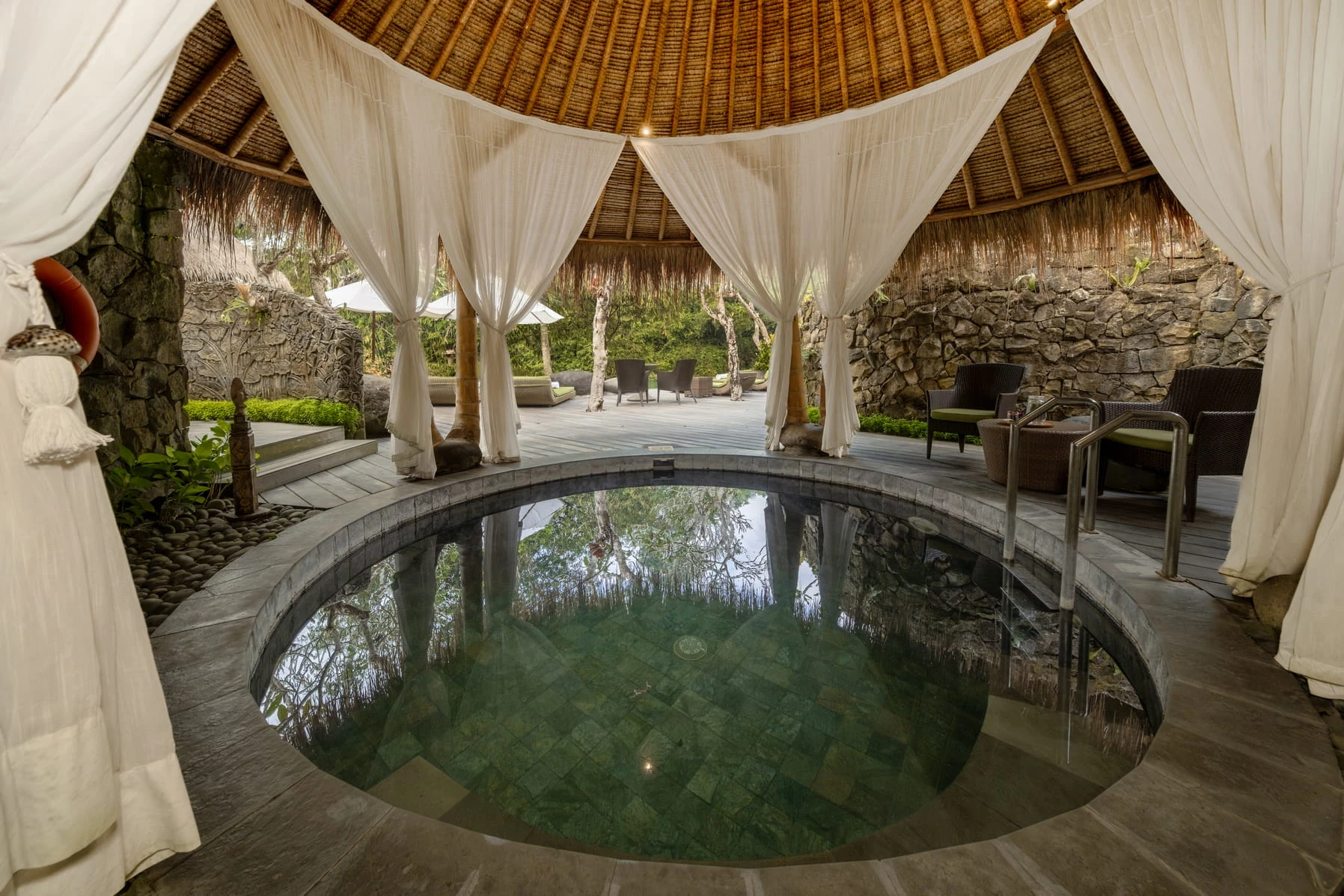 A round indoor water pool beneath a thatched roof and white curtains at Fivelements.