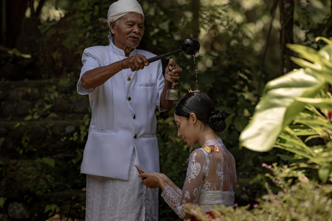 A priest pouring water during a blessing at Mandapa, with a participant seated in prayer.