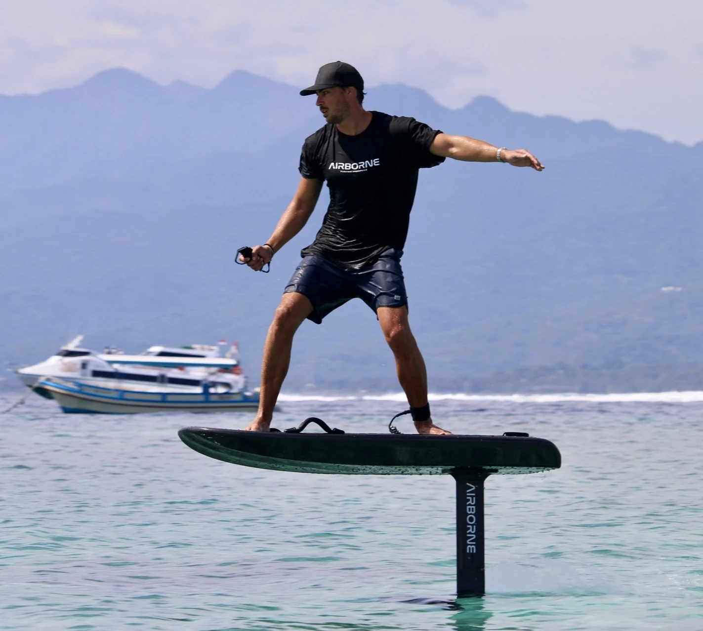 A rider balances on an electric hydrofoil board with Bali’s mountains in the distance