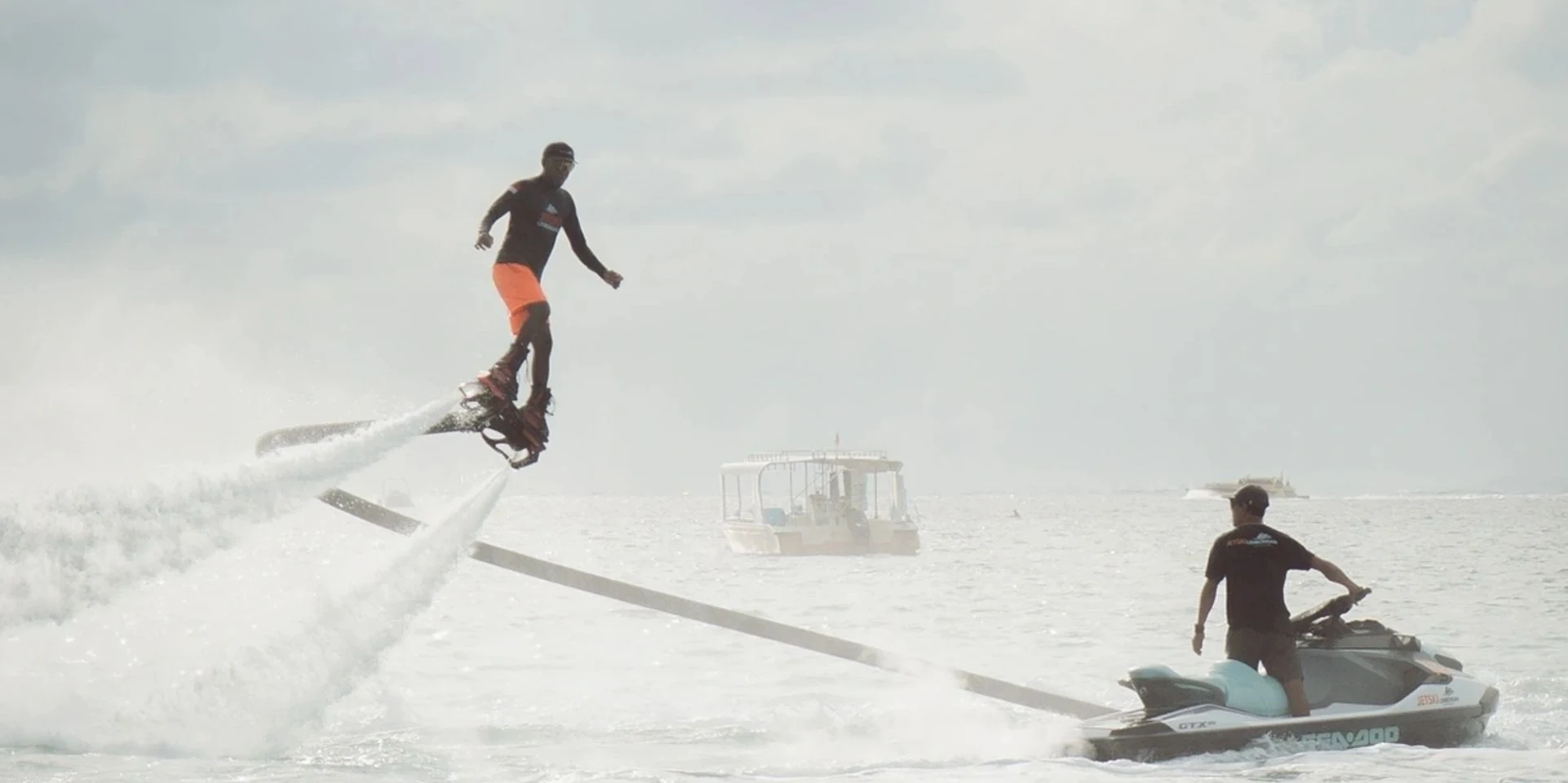 A rider rises above Jungutbatu Lagoon on a water-powered flyboard while a jet-ski operator controls the tow