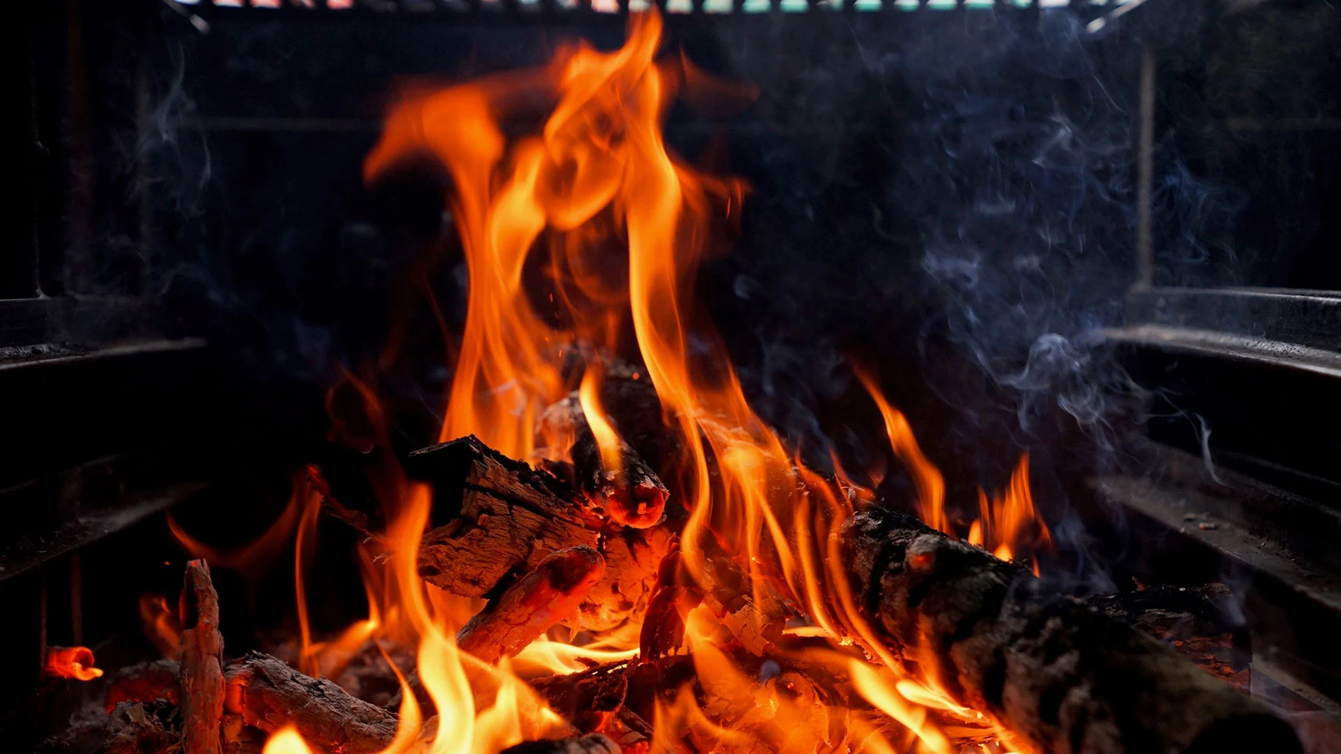 Orange flames and glowing wood in a dark hearth
