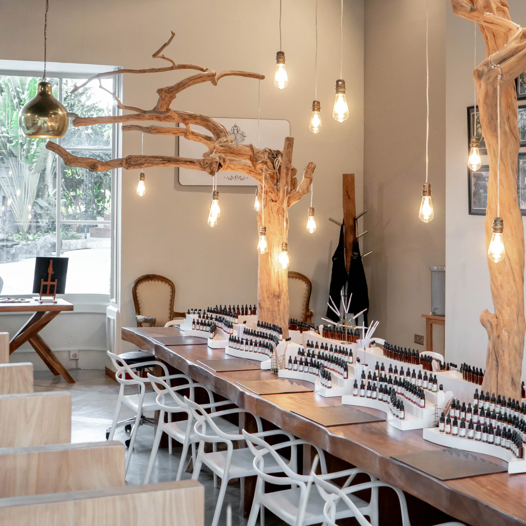 The light-filled L’Atelier perfume studio with wooden worktables, fragrance bottles and hanging lamps.
