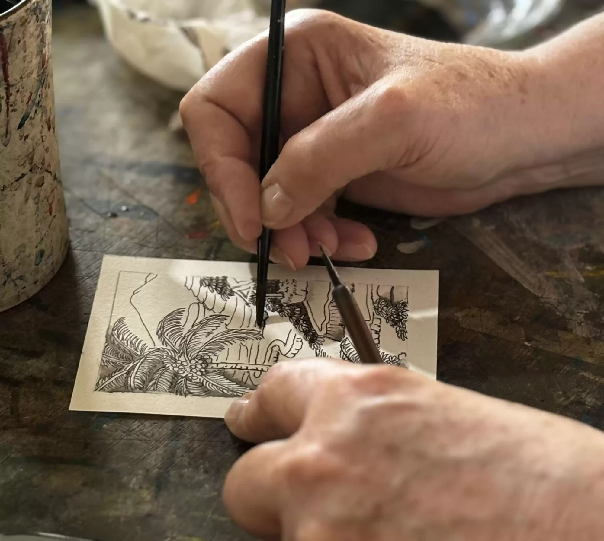 Close-up of a hand adding fine ink detail to a small Keliki-style Balinese painting.