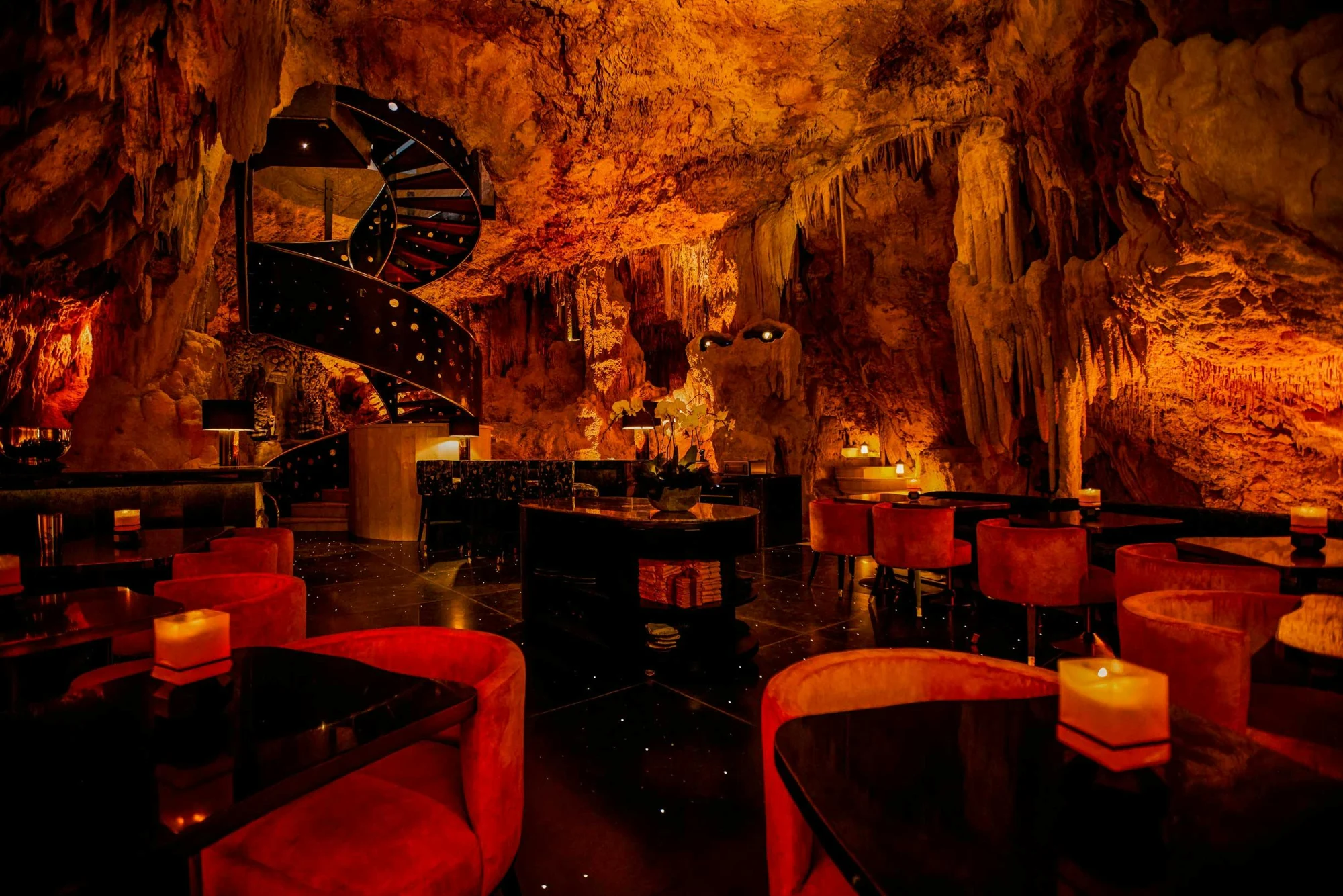 Candlelit tables and a spiral staircase inside The Cave’s natural limestone dining room.