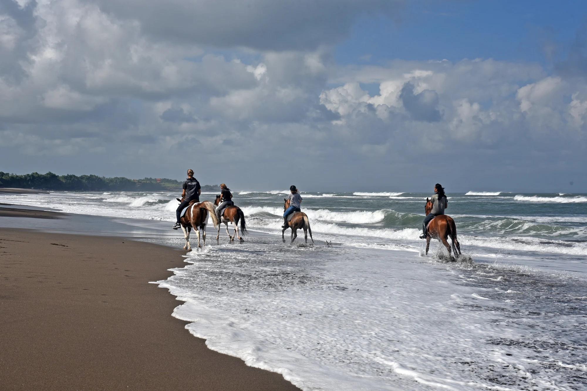Riders and horses on the dark-sand beach at Kedungu, Tabanan.