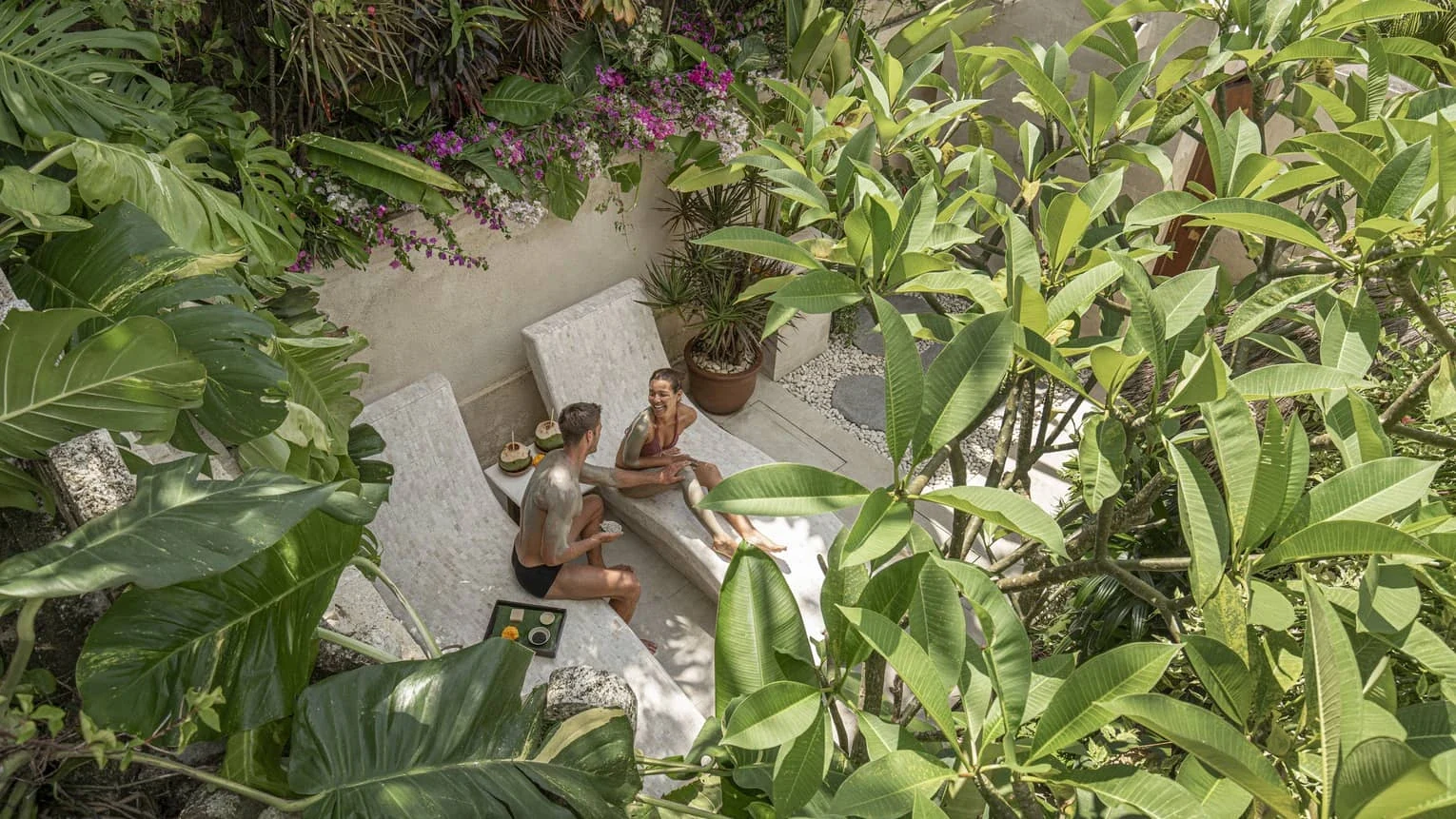A couple relaxes in the Healing Village Spa’s secluded Longevity Garden amid dense tropical greenery.