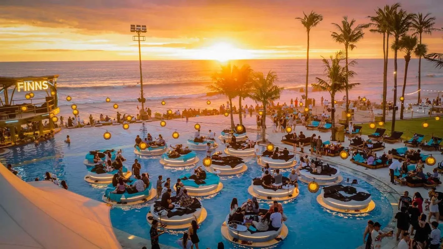 FINNS Beach Club pools and palm-lined oceanfront at sunset.