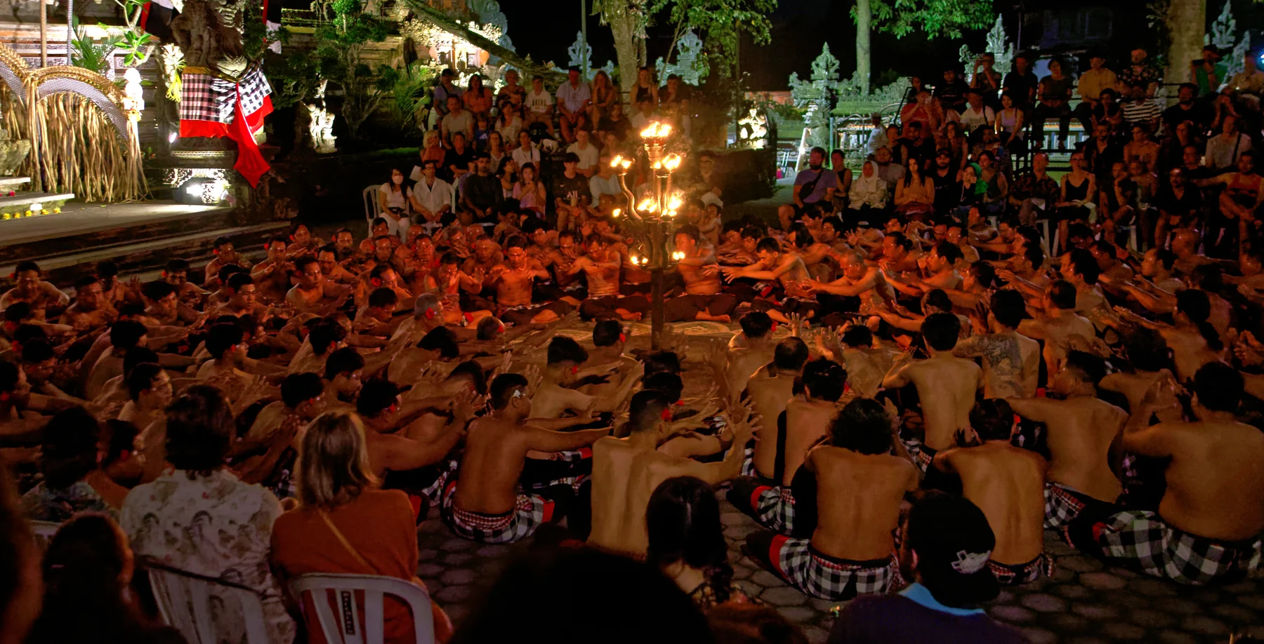 A large circle of Kecak performers gathers around a lit central lamp at Pura Dalem in Ubud.