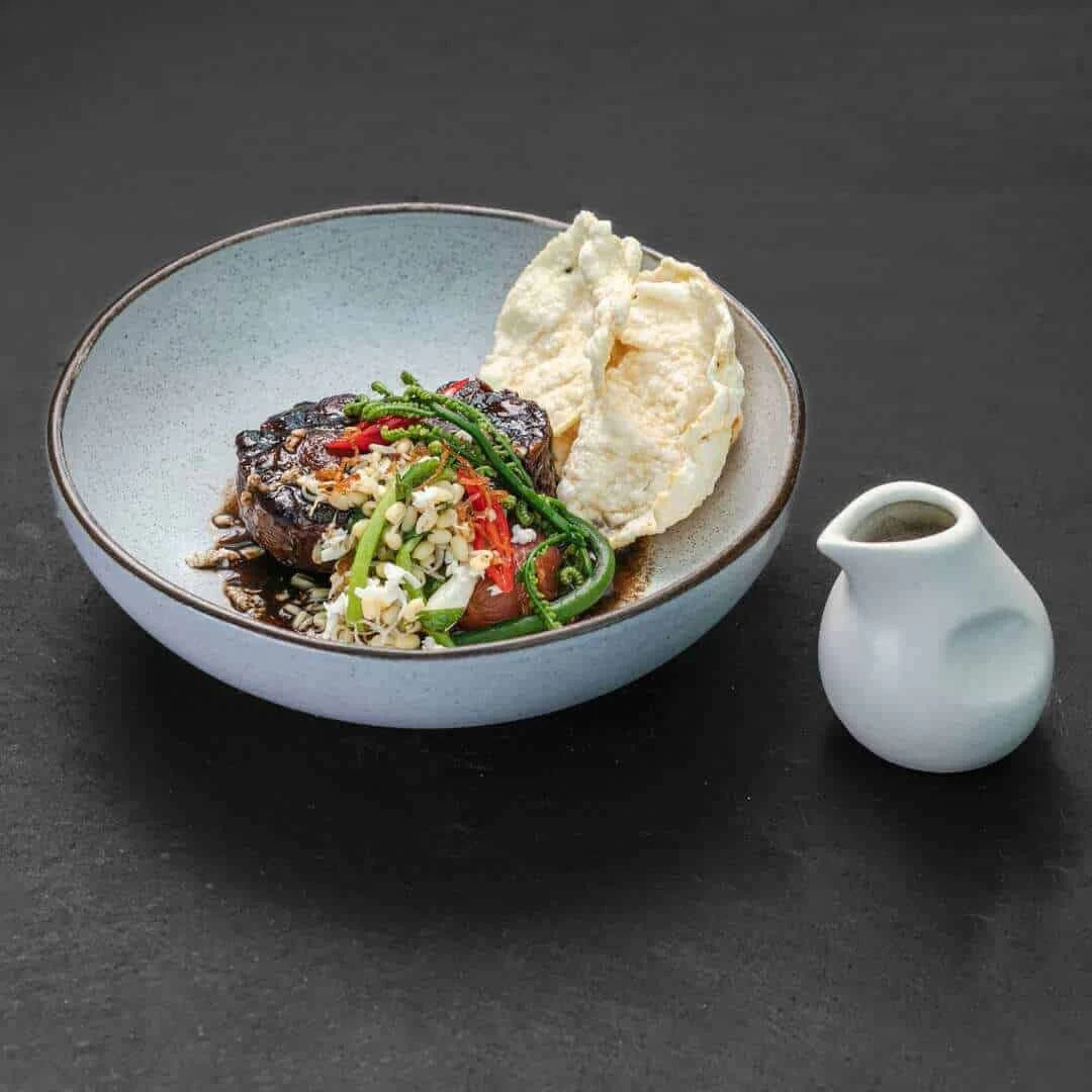 A composed dish with colourful garnishes, crackers and a small sauce jug at Merah Putih.