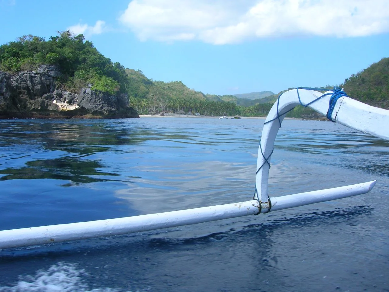An outrigger boat floats beside a rocky, tree-lined snorkeling coast at Nusa Penida.