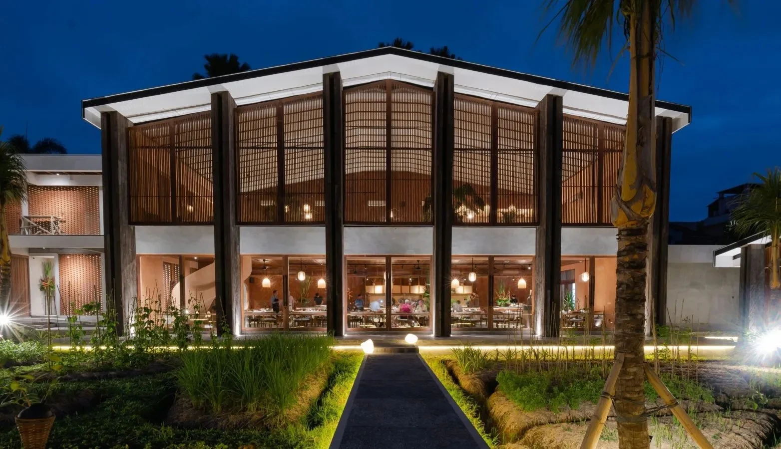 Syrco Basè restaurant illuminated at dusk, framed by its kitchen garden.
