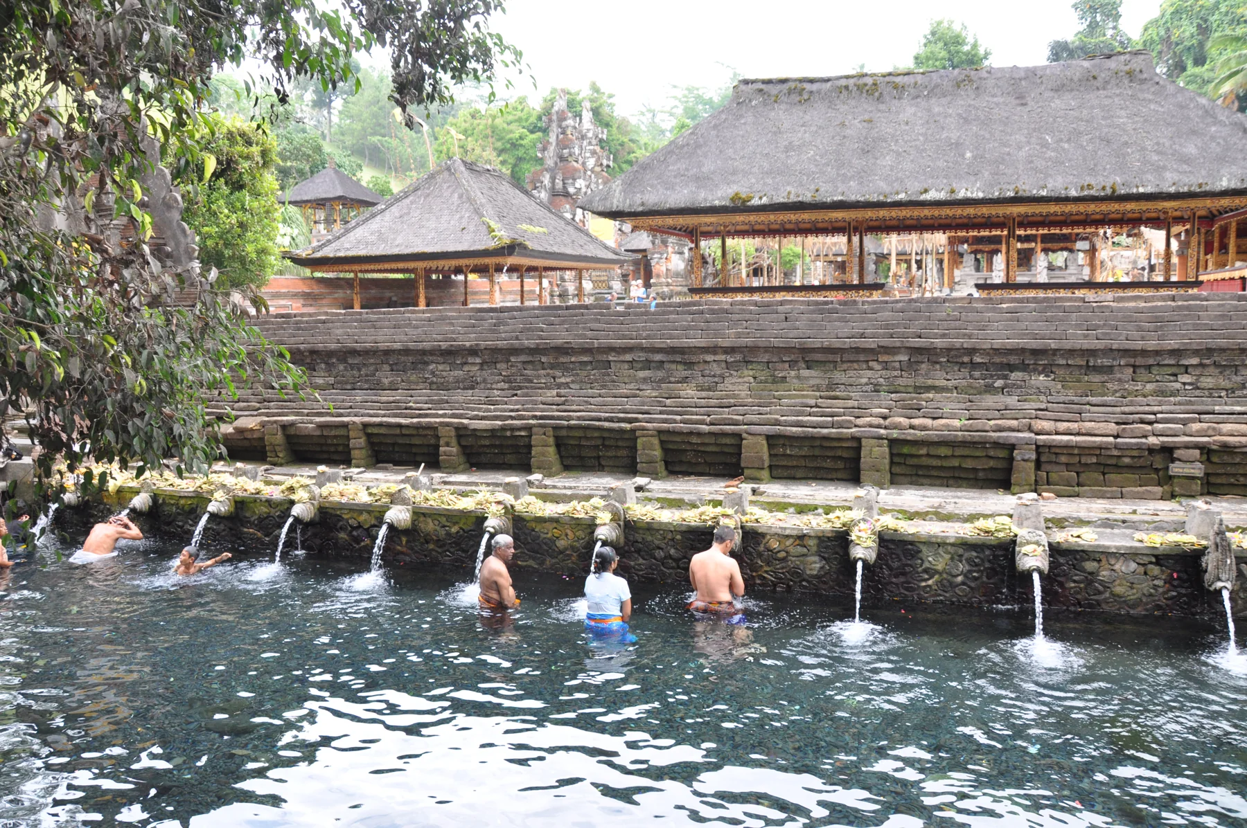 Visitors stand beneath stone water spouts in the purification pool at Tirta Empul temple, Bali.