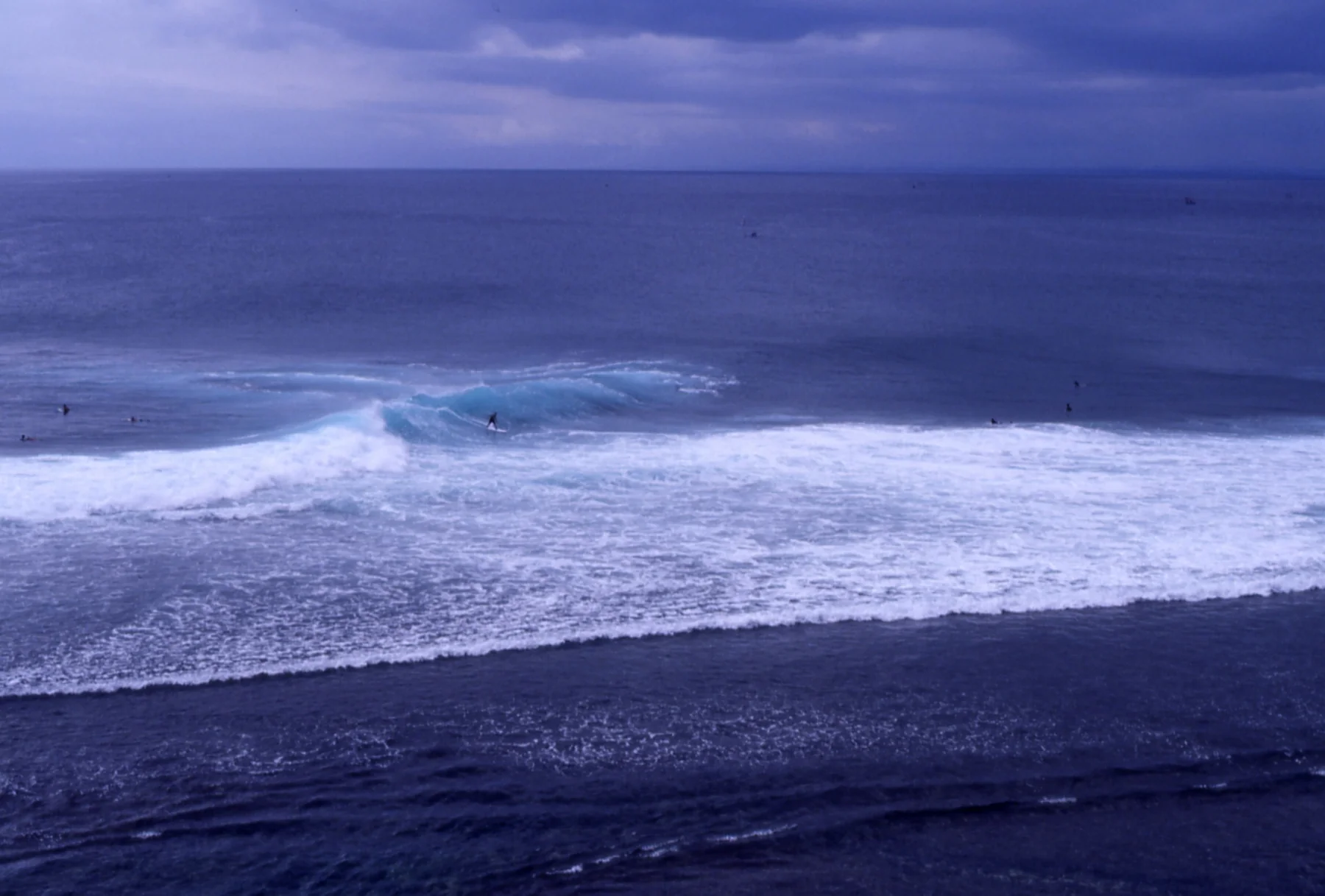Lines of breaking surf roll toward the dark shoreline at Uluwatu, Bali.