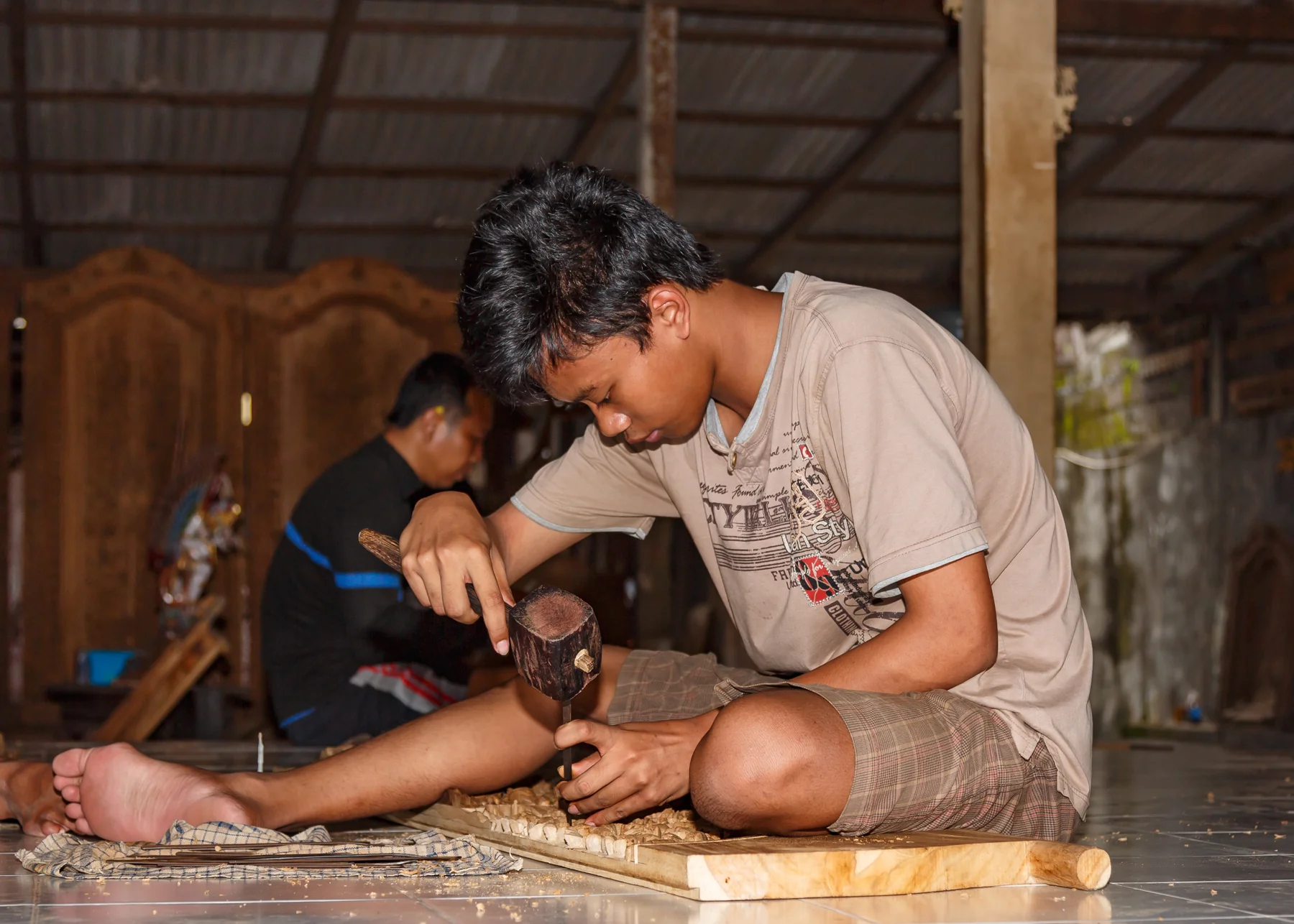 A woodcarver uses a mallet and chisel to carve a wooden panel in Singapadu, Bali.