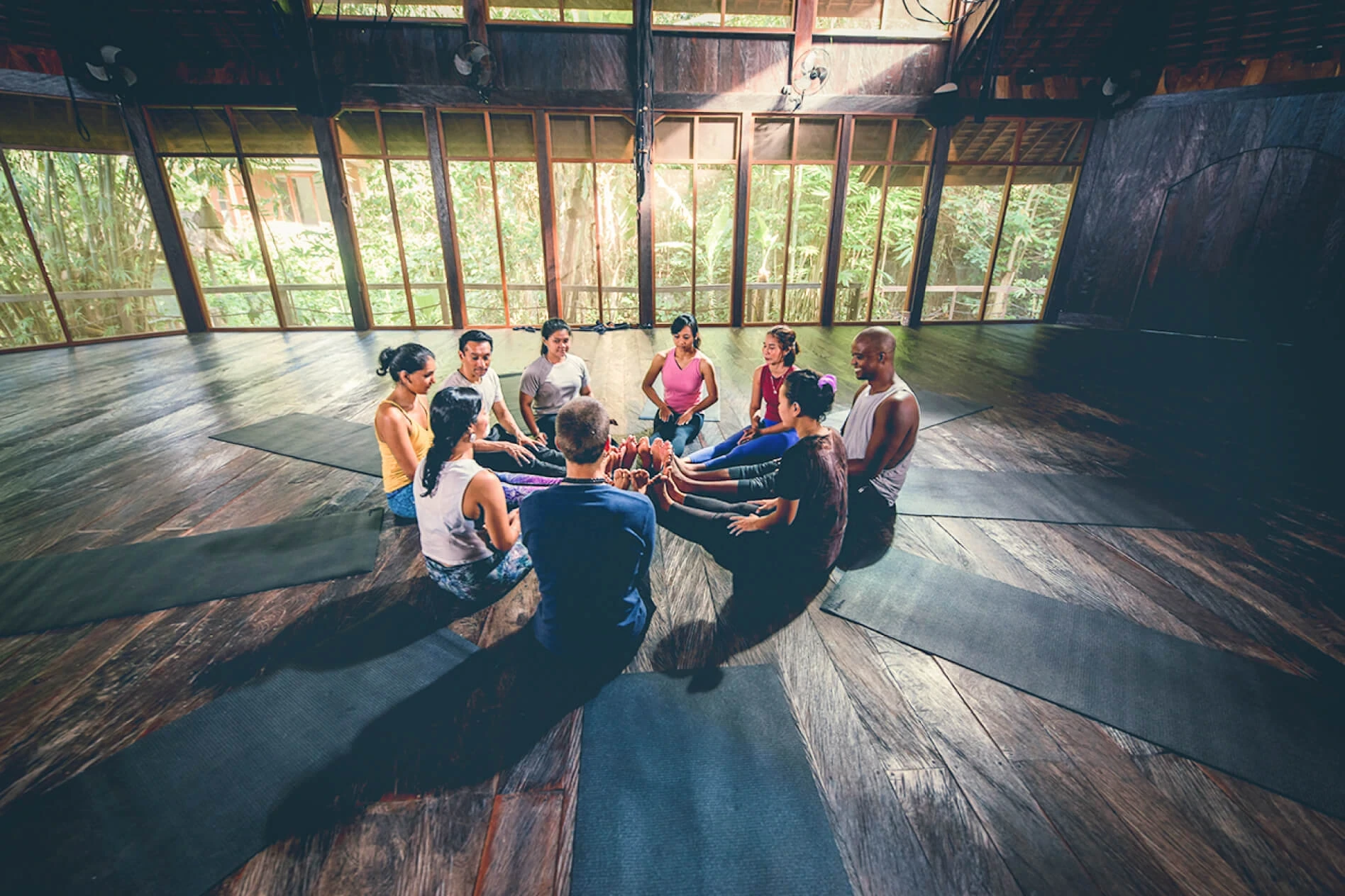 Guests sit in a circle on the timber floor of a sunlit studio at The Yoga Barn in Ubud.