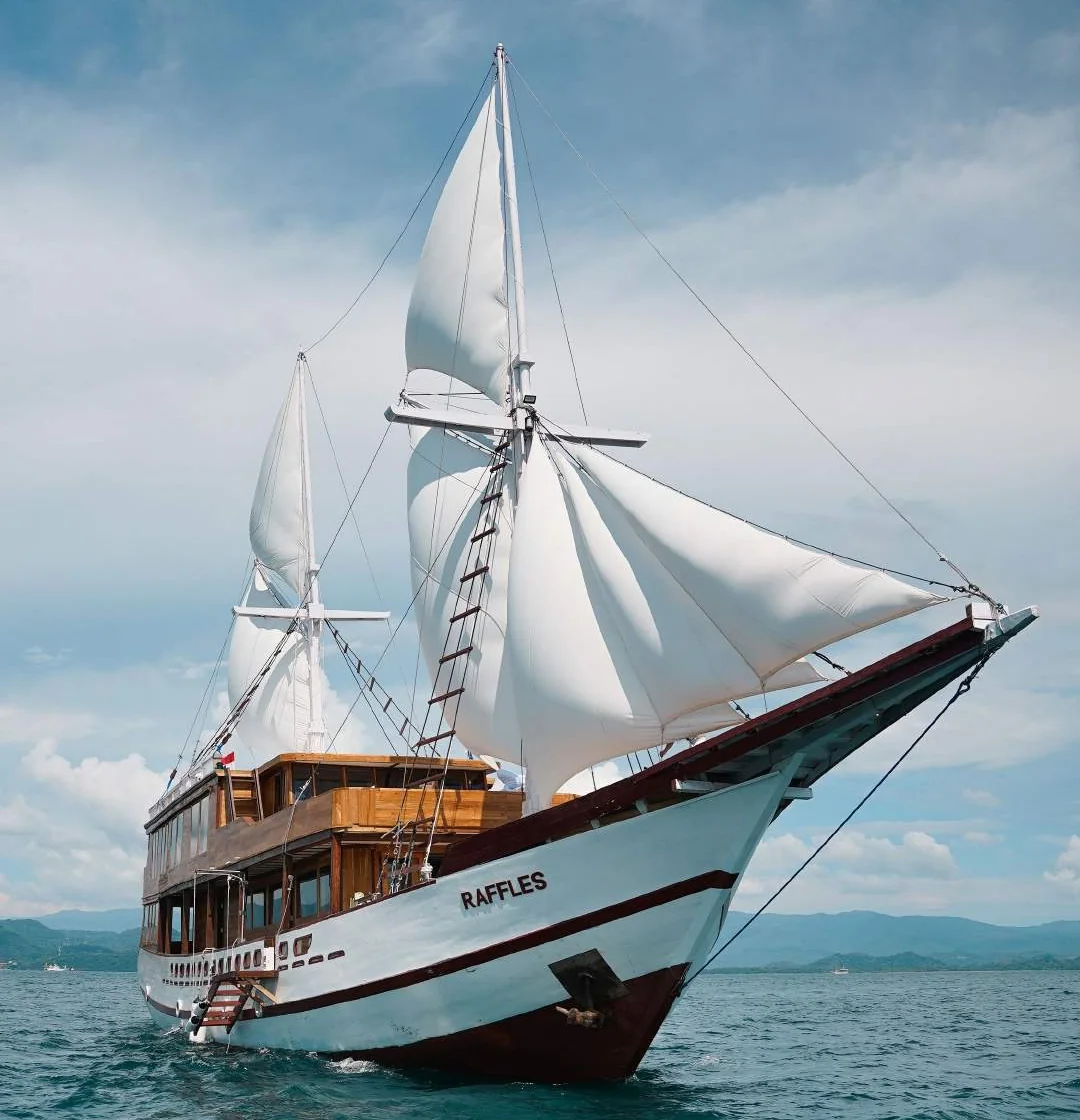 Raffles sailing yacht with white sails raised on blue water